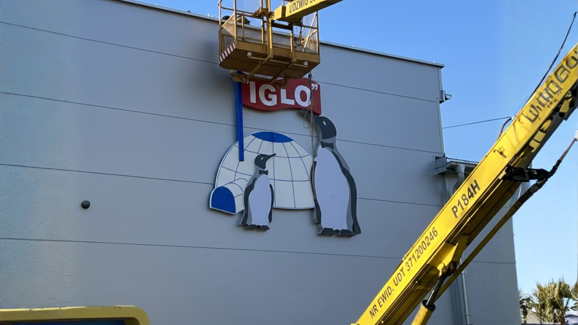 Montaż reklamy zewnętrznej na hali produkcyjnej – instalacja dużego szyldu firmowego z logotypem IGLO